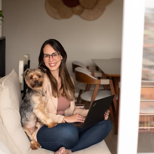 Júlia em casa com seu cachorro, sentada no sofá com o notebook no colo